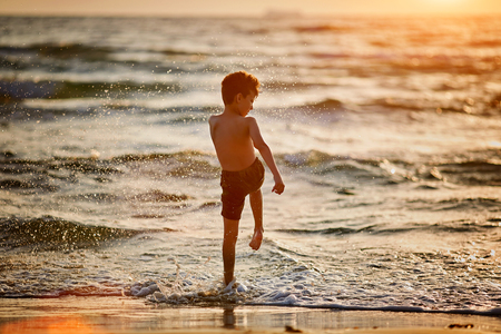 Boy child is running out of water on a sea beach at sunset, cinematic steadicam shotの写真素材