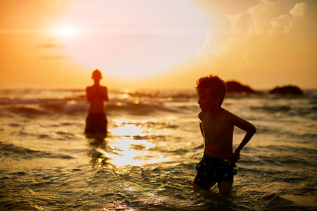 Carefree brothers standing in sea against clear sky during sunset.の写真素材