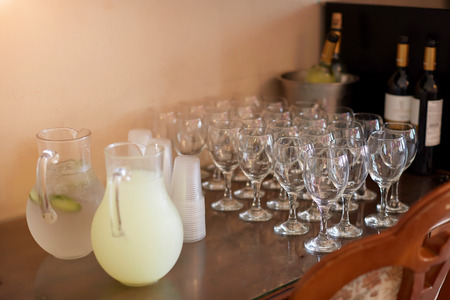 Rows of wine glasses and plastic cups with the beverages on a wooden table in a partyの写真素材