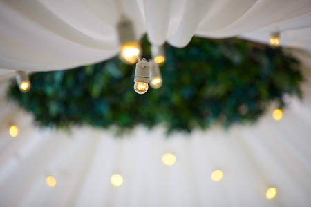 Wedding decorations. Decoration of the hall, restaurant. White tablecloth on Round table. Cutlery. Presidency of newlyweds. candles are burning. Flower compositions on table. Garland of light bulbs.の写真素材