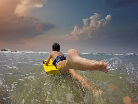 Happy baby boy - young surfer ride on surfboard with fun on sea waves. Active family lifestyle, kids outdoor water sport lessons and swimming activity in surf camp. Summer vacation with child.の写真素材