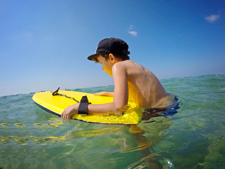 Teenager boy surfing on tropical beach in Asia. Child on surf board on ocean wave. Active water sports for kids. Kid swimming with body board. Young surfer in exotic sea. Swim and eye wear for kids.の写真素材