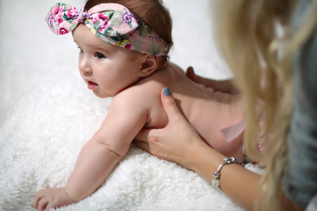 Young mother teaches to crawl a little baby on the bed with a white sheet. Concept of education and child development. Flat lay, top view.の写真素材