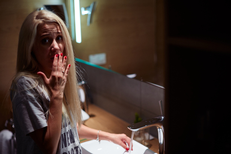 Frightened woman standing in the tub behind the curtain. Scared girl cover her mouth with palm. Horror in bathroom.の写真素材