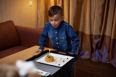 Little smiling child boy blowing birthday celebration sweet cake candle fireの写真素材