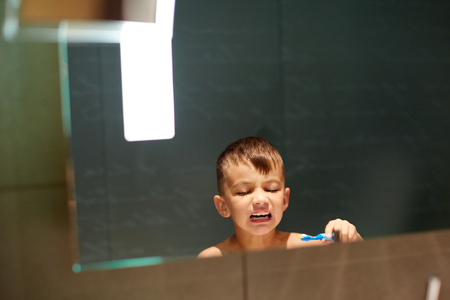 Portrait view of a young man brushing his teeth in a home bathroom, looking at his own reflection getting , home interior. Health and well being teeth care and grooming, indoorsの写真素材