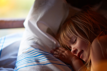 Closeup profile portrait of beautiful blond Caucasian girl with closed eyes near a window with white curtains.の写真素材