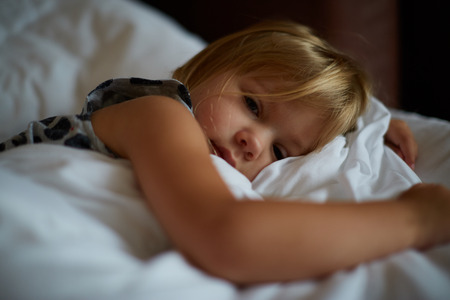 Cute little blond caucasian girl awakening at bed in morning. Child wake up early to go to school. Stretching and yawning. Healthy sleeping. Children healthcare.の写真素材