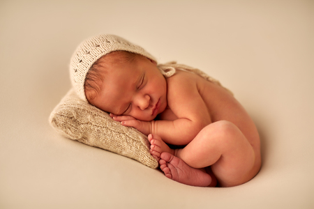 Adorable baby in knitted hat sleeping on small pillow on cream backgroundの写真素材