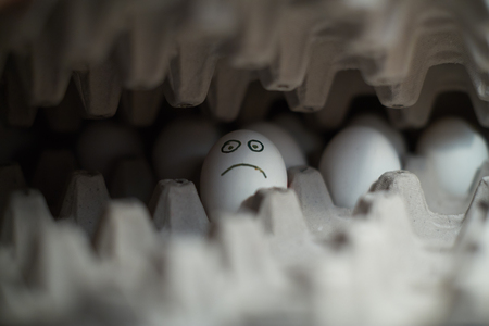 Lonely white egg with sad face in a boxの写真素材