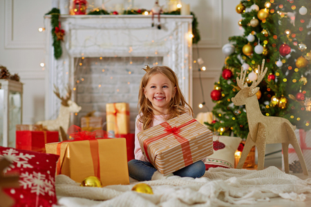 Wonderful laughing little girl sitting on plaid with gift boxes around and looking happy with Christmas timeの写真素材