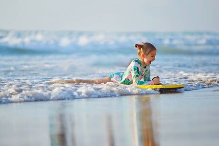 foamy waves of the beautiful autumn sea splashing alongside a charming little girl on surfboardの写真素材