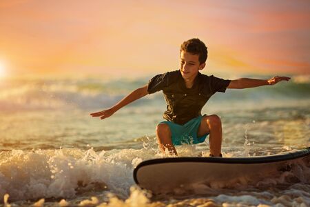 Skilled teenager riding surfboard and balancing along wavy sea at vibrant duskの写真素材