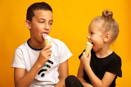 Cute little children eating vanilla ice cream on yellow backgroundの写真素材