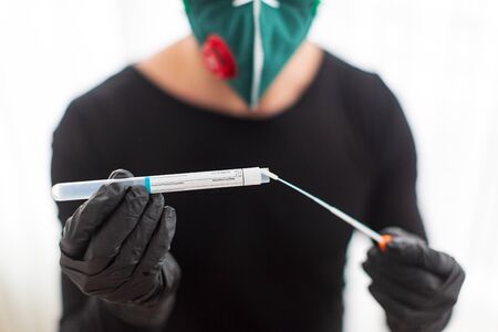man in gloves and a protective mask is preparing to take a sample of biological material for analysis on coronavirus. Pandemic Coveid-19.の写真素材