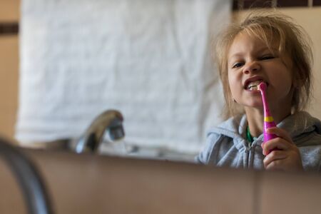 Emotional close up of a cute little girl brushing teeth with electric toothbrush.の写真素材