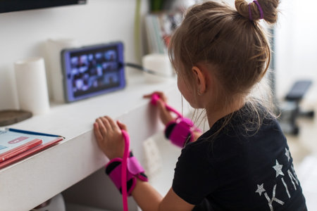 Pretty young girl in sportswear watching online video on laptop and doing fitness exercises at home....