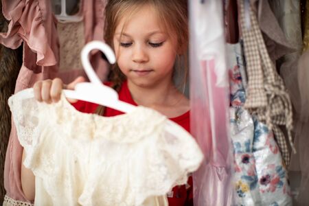 Little child girl choosing her clothes. Kid thinking what to choose to wear in front of many choices of dresses on hangersの写真素材
