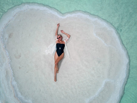 young blonde woman in glasses and black bikini relaxing in the dead sea.