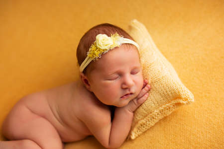 portrait of a beautiful seven day old baby girl. She is sleeping in a curled up fetal position on a yellow blanketの写真素材