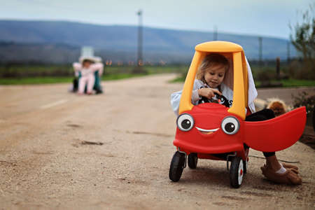 Little adorable toddler girl driving big vintage toy car and having fun with playing outdoors. Gorgeous happy healthy child enjoying warm summer day. Smiling stunning kid playingの写真素材