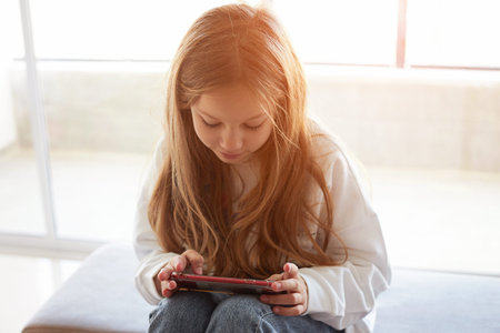 Teen girl checking social media using smartphone at home. Girl relaxing playing mobile games,...