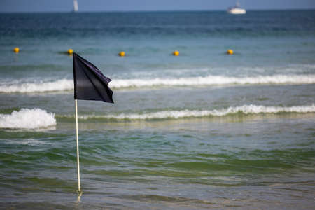 Black warning flag flapping in the wind at stormy weather.Black Flag on the sea shore-warning about dangerous current and waves. Swimming is prohibitedの写真素材