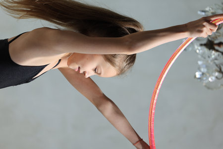 girl gymnast in a black leotard with a with hoop on a grey background. Rhythmic gymnastics conceptの写真素材