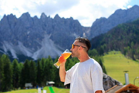 A man enjoys a beer, taking in a stunning mountain view, surrounded by natures beautyの写真素材