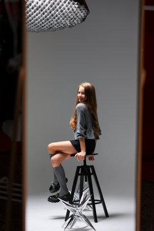 A Trendy Studio Portrait Capturing the Essence of a Young Woman Sitting Gracefully on a Stoolの写真素材