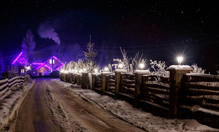 Winter night scene. starry sky over snowy road and wooden cottage, Christmas holidays concept. rural winter landscapeの写真素材