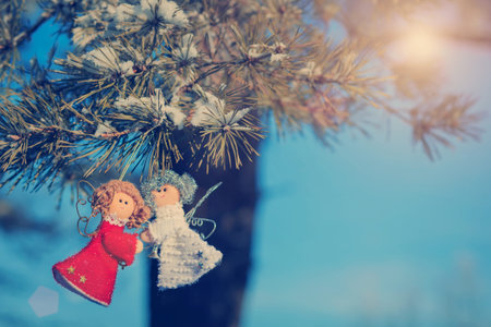 Two small dolls angels with sprig of pine sprinkled with snow. Christmas decorations and toys for Christmas tree. small red dolls angels. winter selebrations beautiful backgroundの写真素材