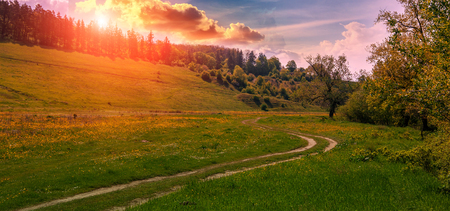 Rural dirt road at sunset. Green grass field and mountain landscape with fantastic clouds. Beauty in natureの写真素材