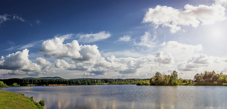 fantastic view. dazzling sun enlightens trees and clouds in the sky. Wonderful summer day. Fantastic views of the Lake in the forest. under sunlight. Dramatic and picturesque scene. artistic images.の写真素材