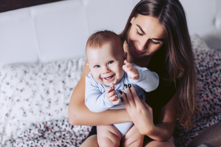 Young mother with the small child sit on a bed and smileの写真素材