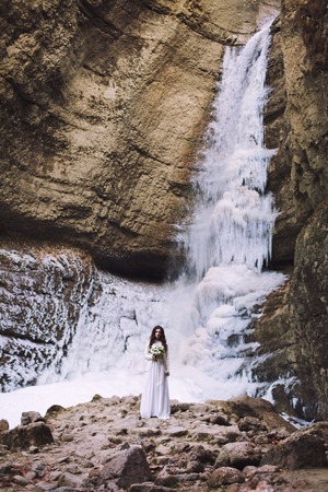 A girl in a wedding dress with a bouquet of flowers on a background of a glacier and mountainsの写真素材