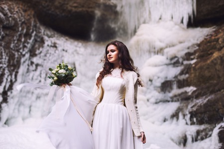 Beautiful young girl in a wedding dress against a background of a glacier in the mountainsの写真素材