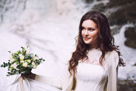 Beautiful bride holding a bouquet of flowers from roses on the background of a glacierの写真素材