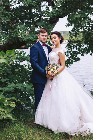 Bride hugging groom on the river bank under a treeの写真素材