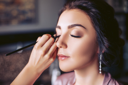 Make-up artist puts make-up on the eyes of a young brideの写真素材