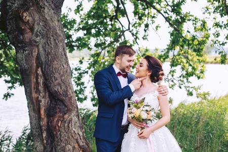 The bride and groom are smiling under a big tree on the river bankの写真素材