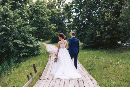 The bride and groom walk along a wooden path among the trees in the parkの写真素材