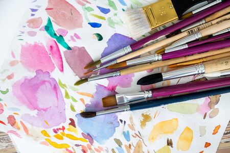 Multiple painting brushes laying on colorful watercolor backgroundの写真素材