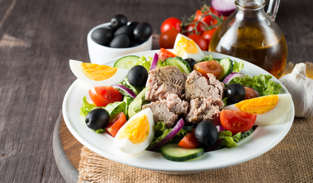 Fresh fish tuna salad made of tomato, ruccola, tuna, eggs, arugula, crackers and spices. Caesar salad in a white bowl on a wooden backgroundの写真素材