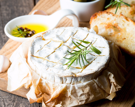 Baked camembert cheese. Fresh Brie cheese and a slice on a wooden board with nuts, honey, rosemary, baguette bread grilled toasts and leaves. Brie type of cheese. Italian, French cheese.の写真素材