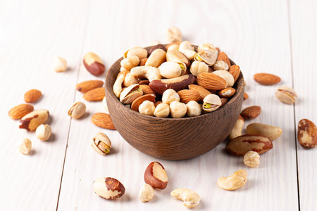 Mix of nuts in wooden bowl on white wooden background. Close up.の写真素材