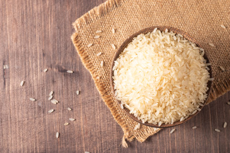 Raw rice in a wooden bowl on burlap and wooden background.の写真素材