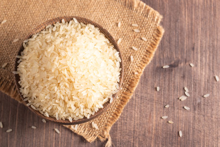 Raw rice in a wooden bowl on burlap and wooden background.の写真素材