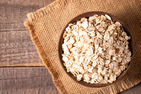 Oat flakes in a wooden bowl on sackcloth and wooden background
