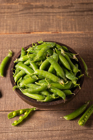 Green peas in a wooden bowl on a wooden background. Selective focus.